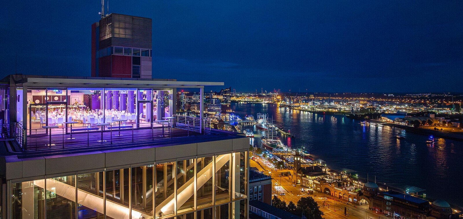 Außenansicht des Penthouse Elb-Panorama bei Nacht mit beleuchteter Dachterrasse und weitem Blick über Elbe, Hafen und die Hamburger Landungsbrücken.