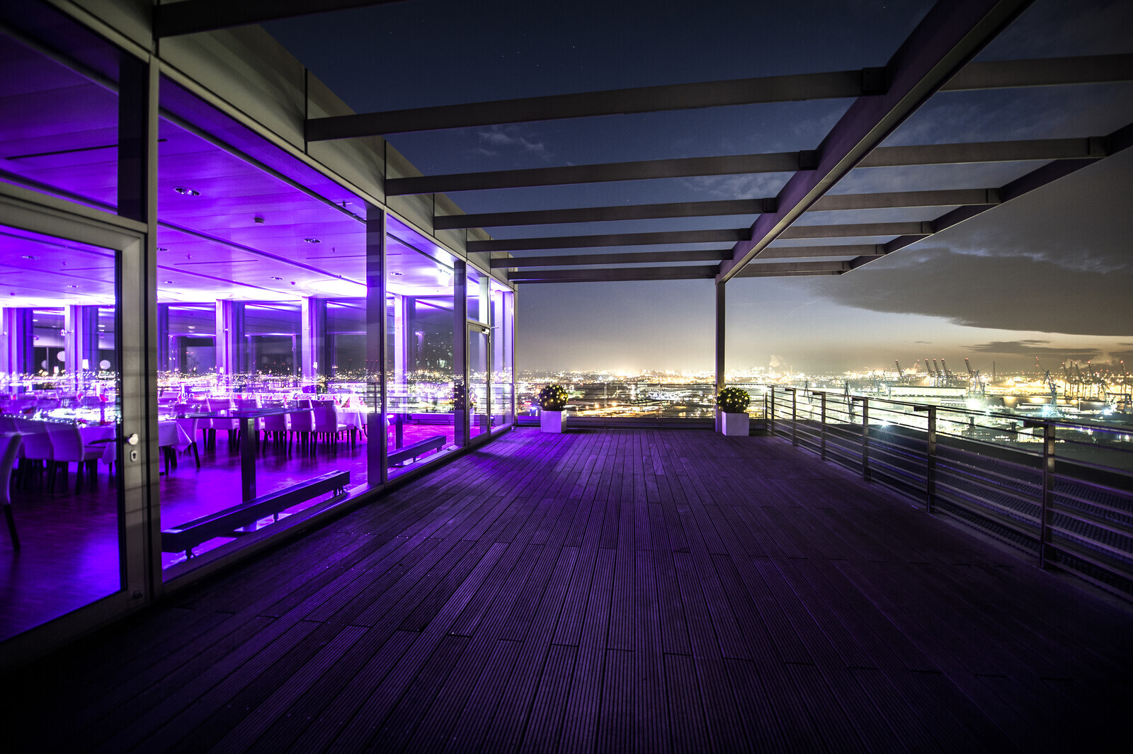 Dachterrasse einer Eventlocation in Hamburg bei Nacht mit bodentiefen Fenstern, violett beleuchtetem Innenraum und weitem Blick über den Hafen.